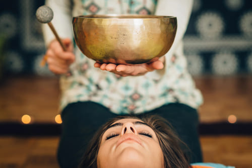 Wellnessmassagen Federleicht, Klangschalenmassage - Über einer Frau wird eine Klangschale gehalten und angeschlagen.